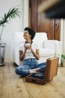 Giovane donna afroamericana seduta a terra ad ascoltare musica dal giradischi, bere caffè — Foto stock
