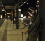 Junge Frau mit Kopfhörer und Tablet wartet nachts am Bahnhof — Stockfoto