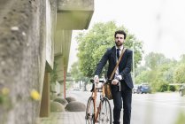 Uomo d'affari con bicicletta passeggiando per strada — Foto stock