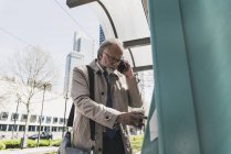 Reifer Geschäftsmann mit Handy und Kaffee zum Mitnehmen in der Stadt an Straßenbahnhaltestelle — Stockfoto