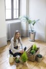 Портрет усміхнена жінка сидячи на підлозі в домашніх умовах і догляд за рослинами — стокове фото