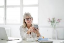 Доросла бізнесменка дивиться на мобільний телефон за столом. — стокове фото