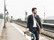 Homme d'affaires avec planche à roulettes et écouteurs marchant sur la plate-forme — Photo de stock
