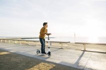 Boy equitação scooter no calçadão da praia ao pôr do sol — Fotografia de Stock