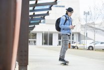 Young man skateboarding in the city, using smartphone, listening music — Stock Photo
