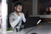 Empresario trabajando en el ordenador portátil en la oficina por la noche - foto de stock