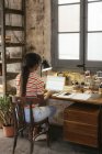 Back view of young woman sitting at desk in a loft working on laptop — Stock Photo