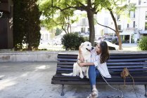 Jovem feliz sentada com seu cachorro no banco da cidade — Fotografia de Stock