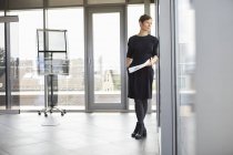 Geschäftsfrau steht im Büro und schaut aus dem Fenster — Stockfoto