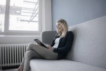 Cheirando empresária sentada no sofá e usando tablet — Fotografia de Stock