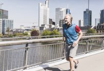 Усміхнена зріла людина з навушниками працює на мосту в місті — стокове фото