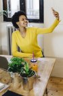 Young african american woman sitting at table and taking selfie — Stock Photo