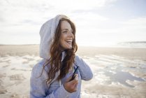 Frau amüsiert sich an einem windigen Strand, trägt Kapuze — Stockfoto