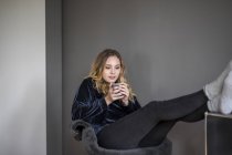 Retrato de mujer joven con bebida caliente en casa - foto de stock