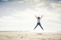 Happy woman having fun at the beach, jumping in the air — Stock Photo