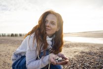Рыжая женщина собирает раковину на пляже — стоковое фото
