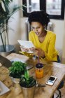 Молодая африканская американка сидит за столом с несколькими переносными устройствами — стоковое фото