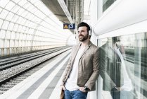 Усміхнений юнак, одягнений у навушники, очікує на платформі станції — стокове фото