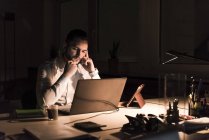 Pensativo hombre de negocios que trabaja en el ordenador portátil en la oficina por la noche - foto de stock