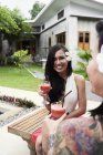 Portrait de femme avec des fleurs dans les cheveux boire un cocktail avec un ami dans le jardin — Photo de stock
