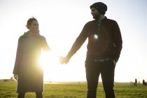 Affectionate young couple standing hand in hand on meadow at sunset — Stock Photo
