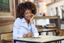 Lächelnde Frau mit Afro-Frisur sitzt im Café im Freien — Stockfoto
