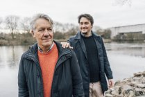 Homme âgé confiant et jeune homme debout au bord de la rivière — Photo de stock