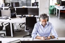 Uomo d'affari maturo seduto alla scrivania in ufficio e utilizzando smartphone — Foto stock