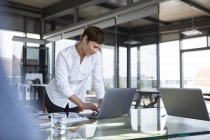 Businesswoman standing at glass table in office using laptop — Stock Photo