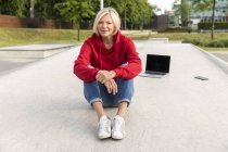 Donna anziana con cappuccio rosso seduta all'aperto con laptop — Foto stock