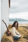 Islandia, mujer con guitarra sentada en el paisaje rural - foto de stock