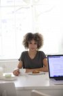 Smiling young woman sitting at table at home with coffee and cake — Stock Photo