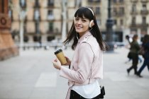 Espanha, Barcelona, mulher sorridente com café, telefone celular e fones de ouvido na cidade — Fotografia de Stock