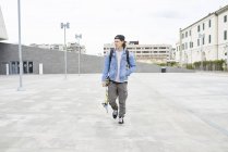 Joven caminando por la ciudad, llevando monopatín - foto de stock