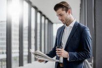 Young businessman standing in a passageway with takeaway coffee and newspaper — Stock Photo