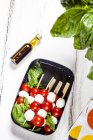 Lunch box of skewered cherry tomatoes and mozzarella cheese balls with basil leaves — Stock Photo