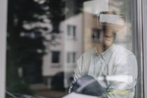 Jeune homme assis à la fenêtre et utilisant des lunettes VR — Photo de stock