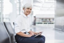 Sorridente donna d'affari anziana seduta in sala d'attesa e utilizzando tablet — Foto stock