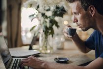 Mittlerer erwachsener Mann sitzt im Café, trinkt Kaffee, benutzt Laptop — Stockfoto