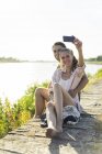 Pareja feliz a orillas del río en verano tomando selfie - foto de stock