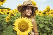 Mujer joven con sombrero de paja sonriendo en el campo de los girasoles - foto de stock