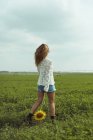 Молода жінка ходить, тримаючи соняшник у зеленому полі — стокове фото