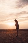 Lonely young woman standing on field at sunset — Stock Photo