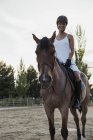 Donna sorridente in casco seduta a cavallo all'aperto — Foto stock