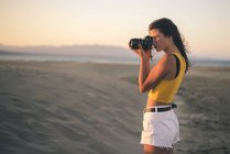Menina adolescente tirando foto com câmera na praia ao pôr do sol — Fotografia de Stock