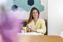Souriante jeune femme dans un café tenant une tasse de café — Photo de stock