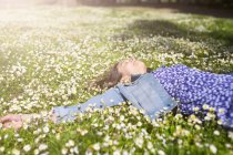 Relajada joven mujer acostada en el prado de flores en el parque - foto de stock