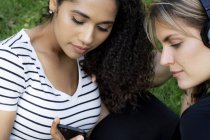 Две девушки в парке слушают музыку, используя смартфон — стоковое фото