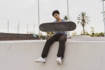 Jeune Chinois assis sur le mur d'un skate park près de la plage — Photo de stock