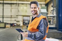 Портрет улыбающегося мужчины, держащего планшет на заводе — стоковое фото